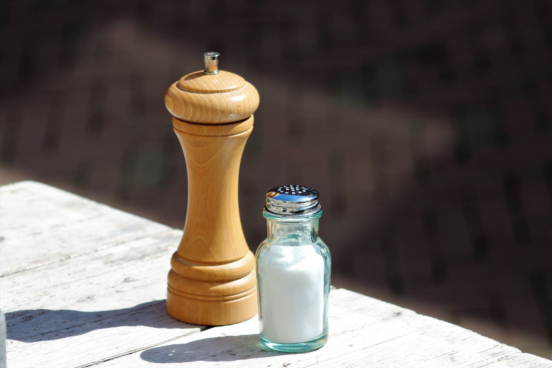 Moulin à poivre en bois clair posé sur une table à côté d’un petit flacon de verre rempli de sel