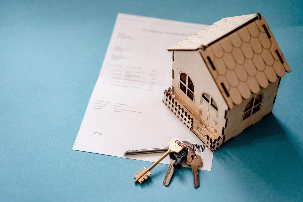 Maquette de maison en bois et clés posées sur un contrat d'assurance habitation