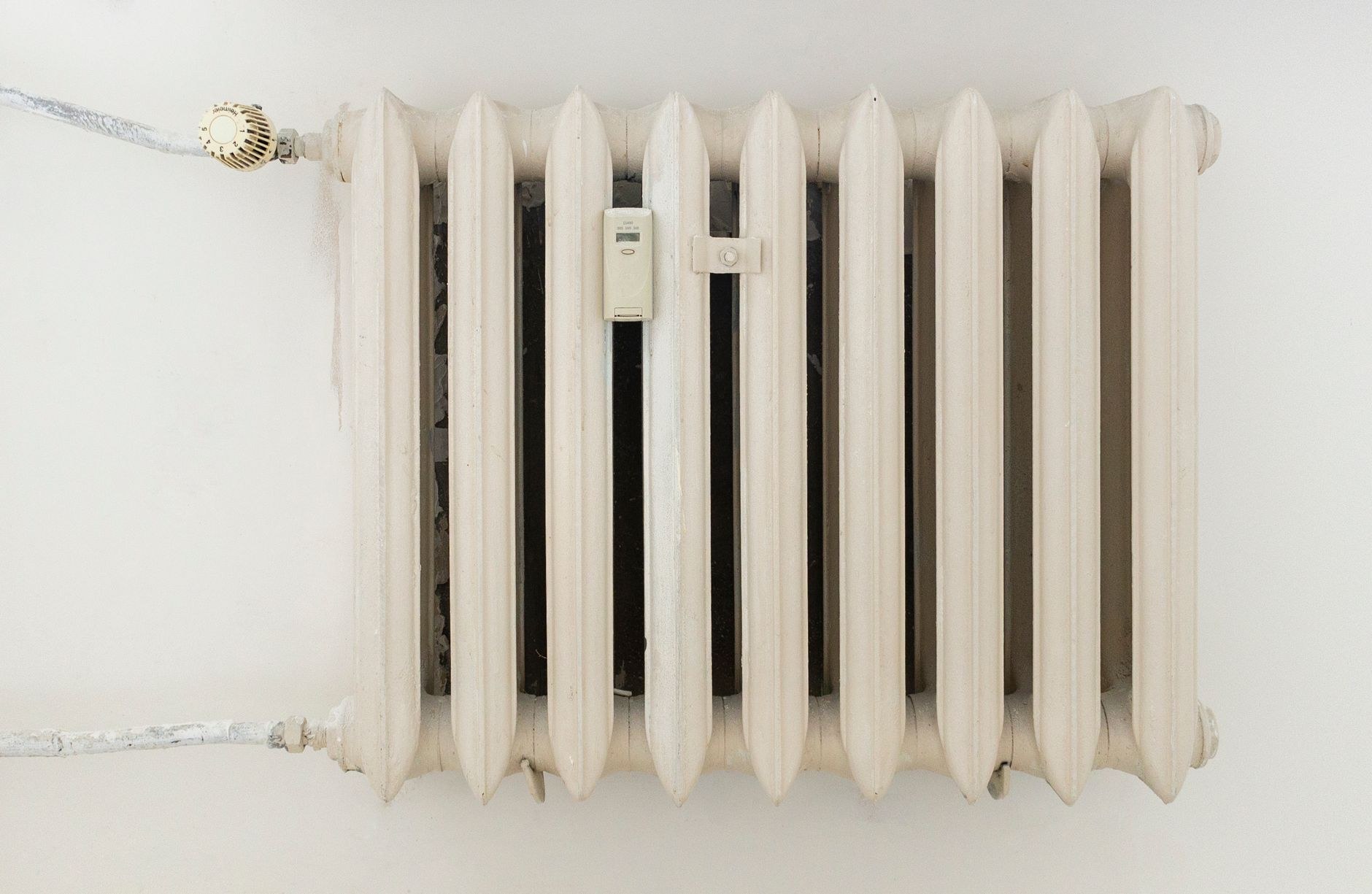 Radiateur en fonte blanc cassé fixé au mur, avec un robinet thermostatique gradué en haut à gauche et un répartiteur de chauffage au centre