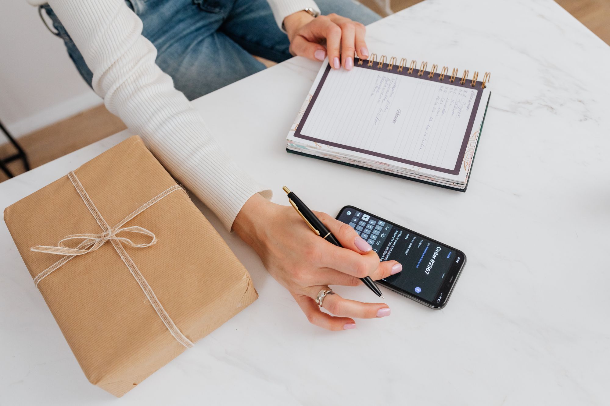 Personne notant son budget dans un carnet à côté d'un smartphone et d'un cadeau emballé