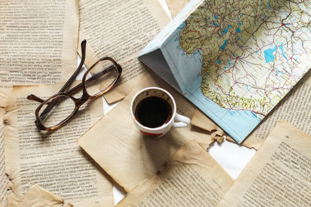 Carte routière dépliée, lunettes, tasse de café et pages anciennes posées sur une table