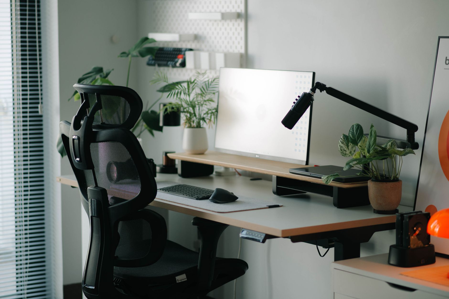 Chaise de bureau ergonomique noire à dossier en résille et appui-tête devant un bureau avec écran et plantes