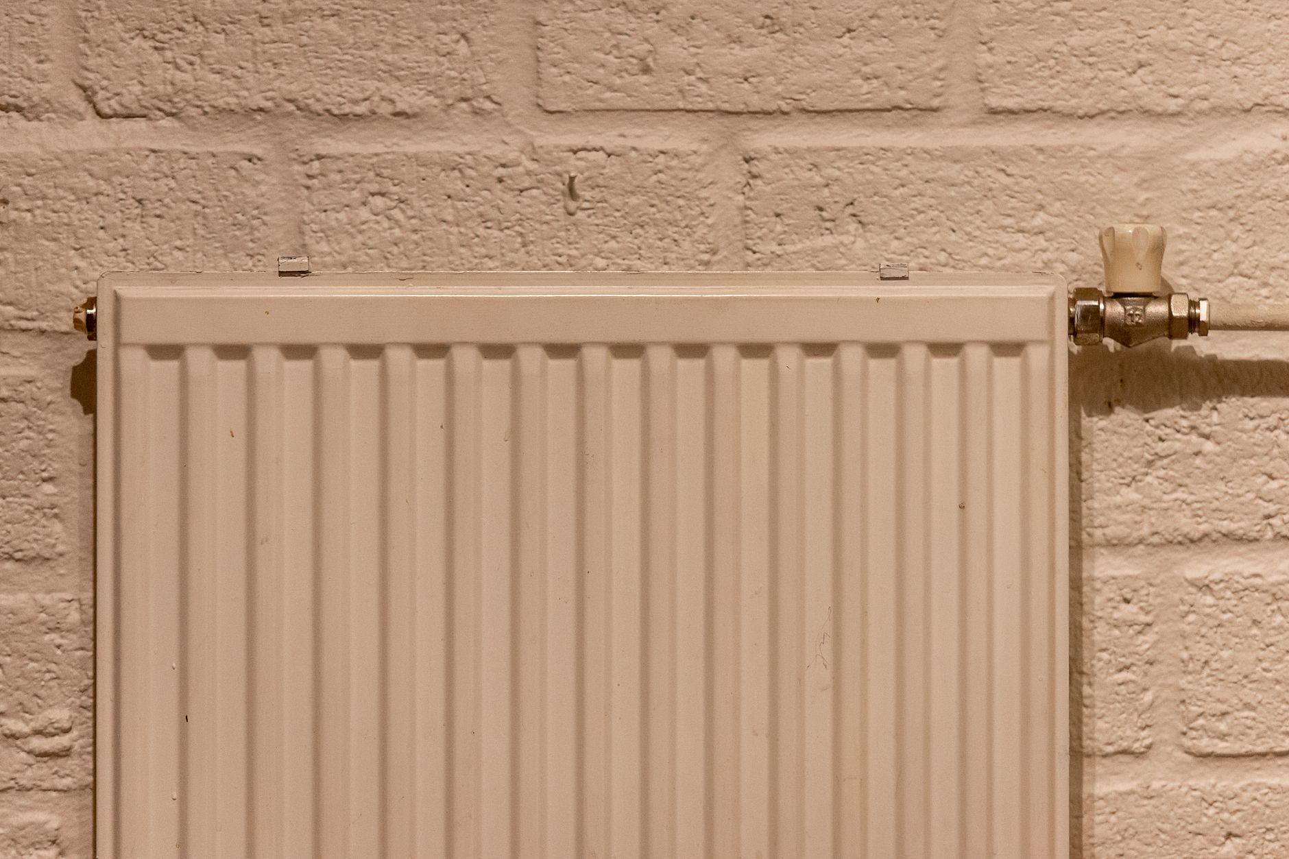 Radiateur blanc à eau chaude fixé sur un mur de briques peintes, avec sa vanne manuelle sur le côté