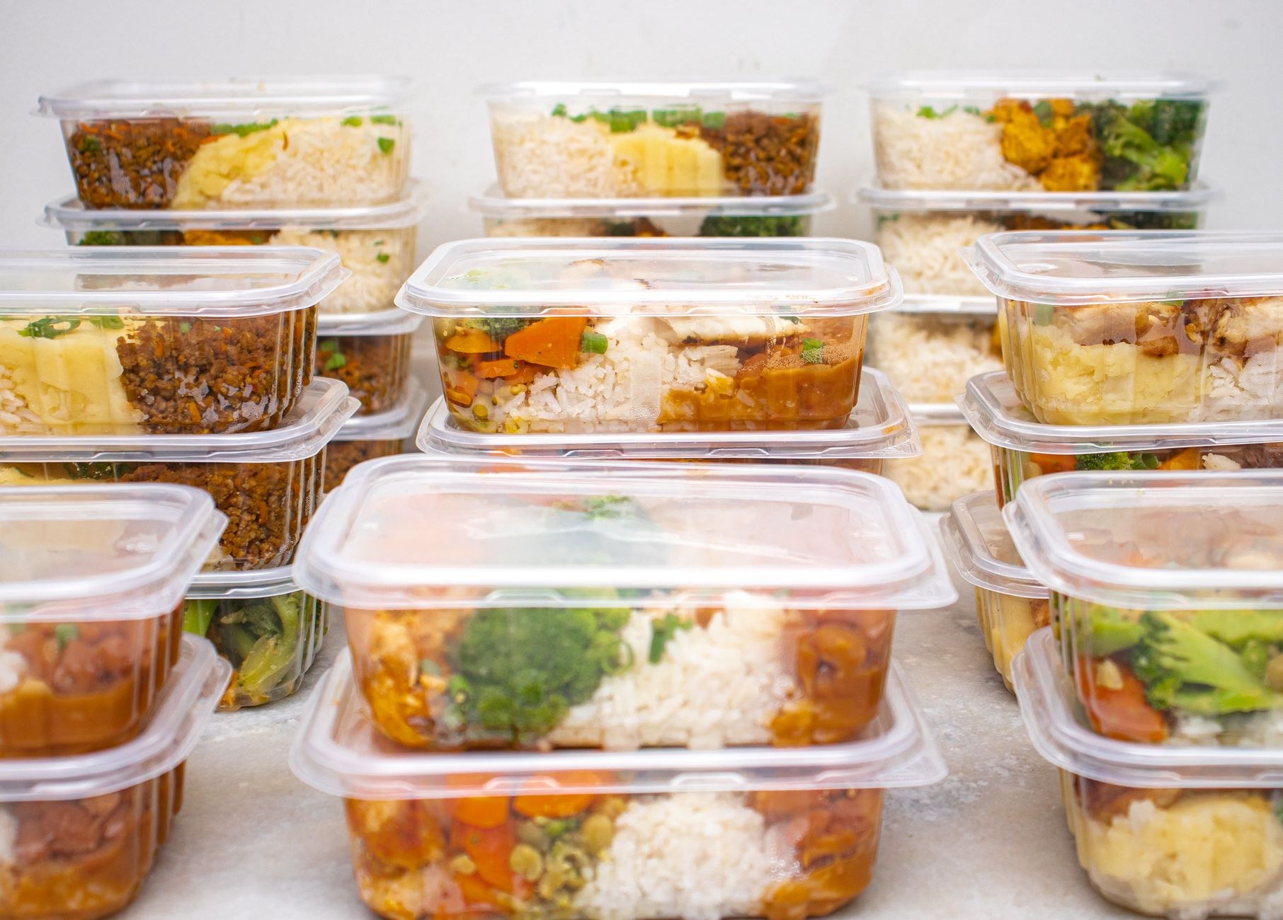 Des dizaines de barquettes transparentes empilées, remplies de riz, légumes et viande, prêtes à être congelées