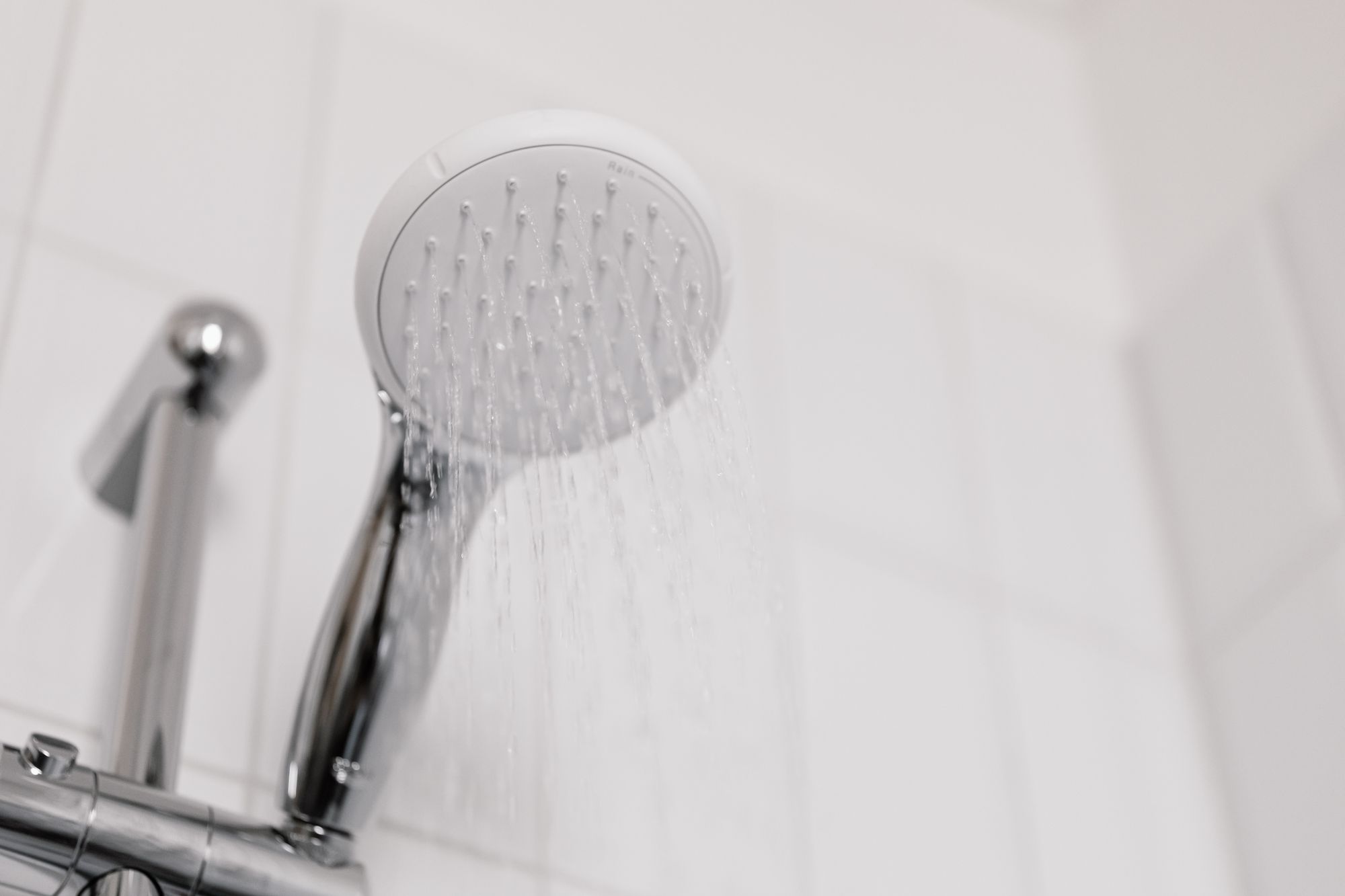 Douchette de salle de bain avec jet d'eau sur un mur carrelé blanc