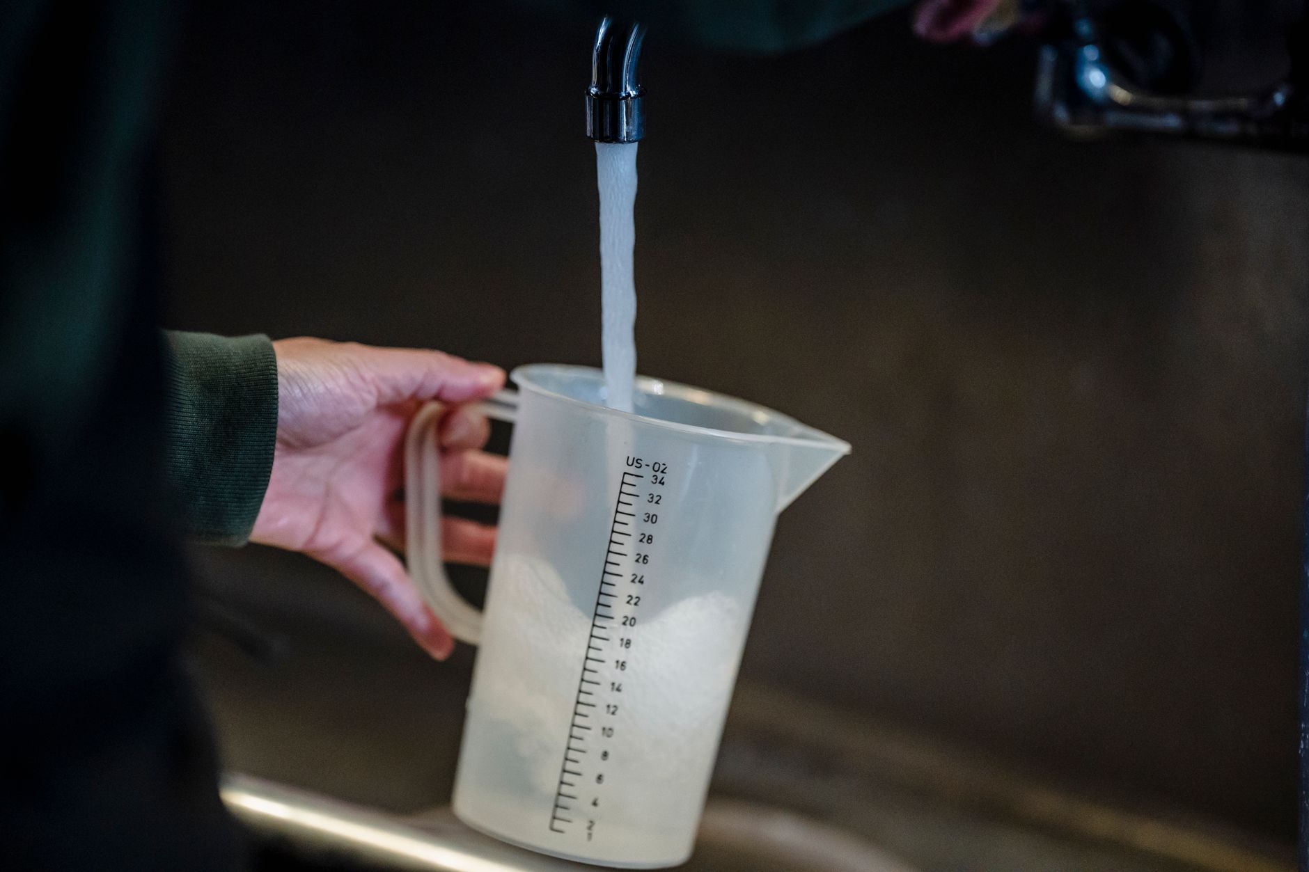 Une main tient un pichet gradué sous un filet d'eau qui sort d'un robinet