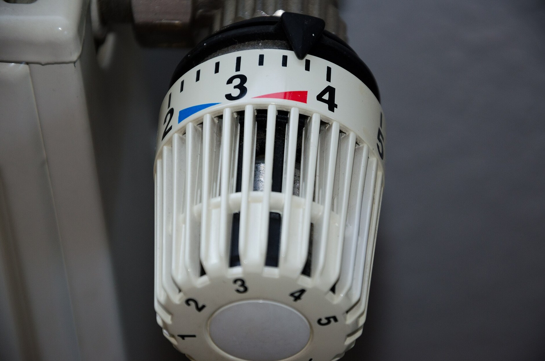 Gros plan sur une tête thermostatique blanche graduée de 1 à 5, vissée sur la vanne d'un radiateur