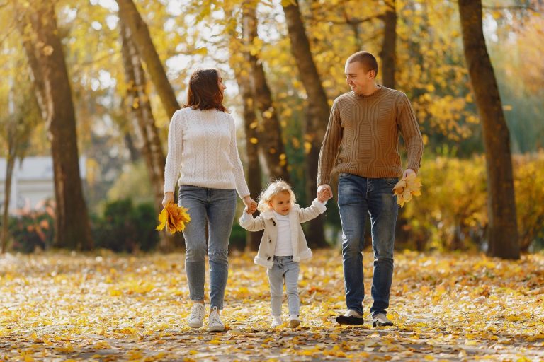 Parents et enfant se promenant main dans la main sur un chemin couvert de feuilles d'automne