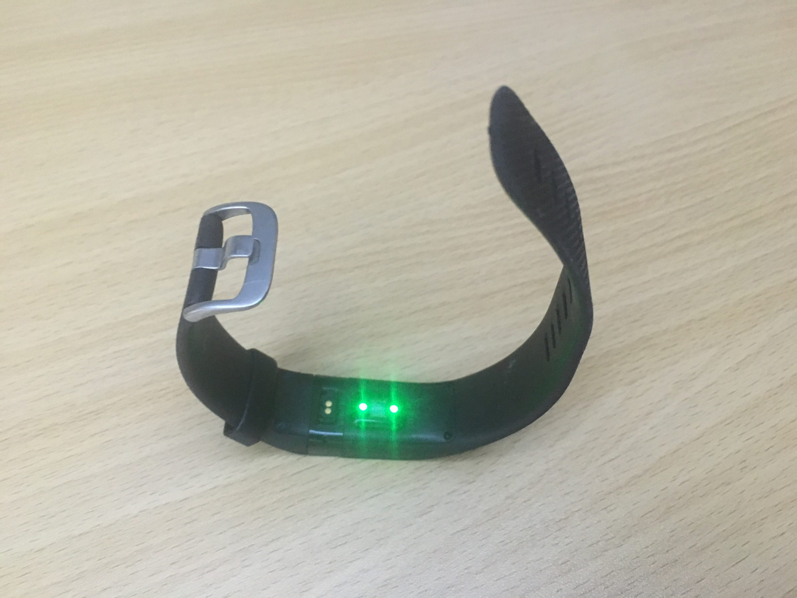 Bracelet d'activité Fitbit Charge HR noir posé sur une table, capteur cardiaque allumé en vert