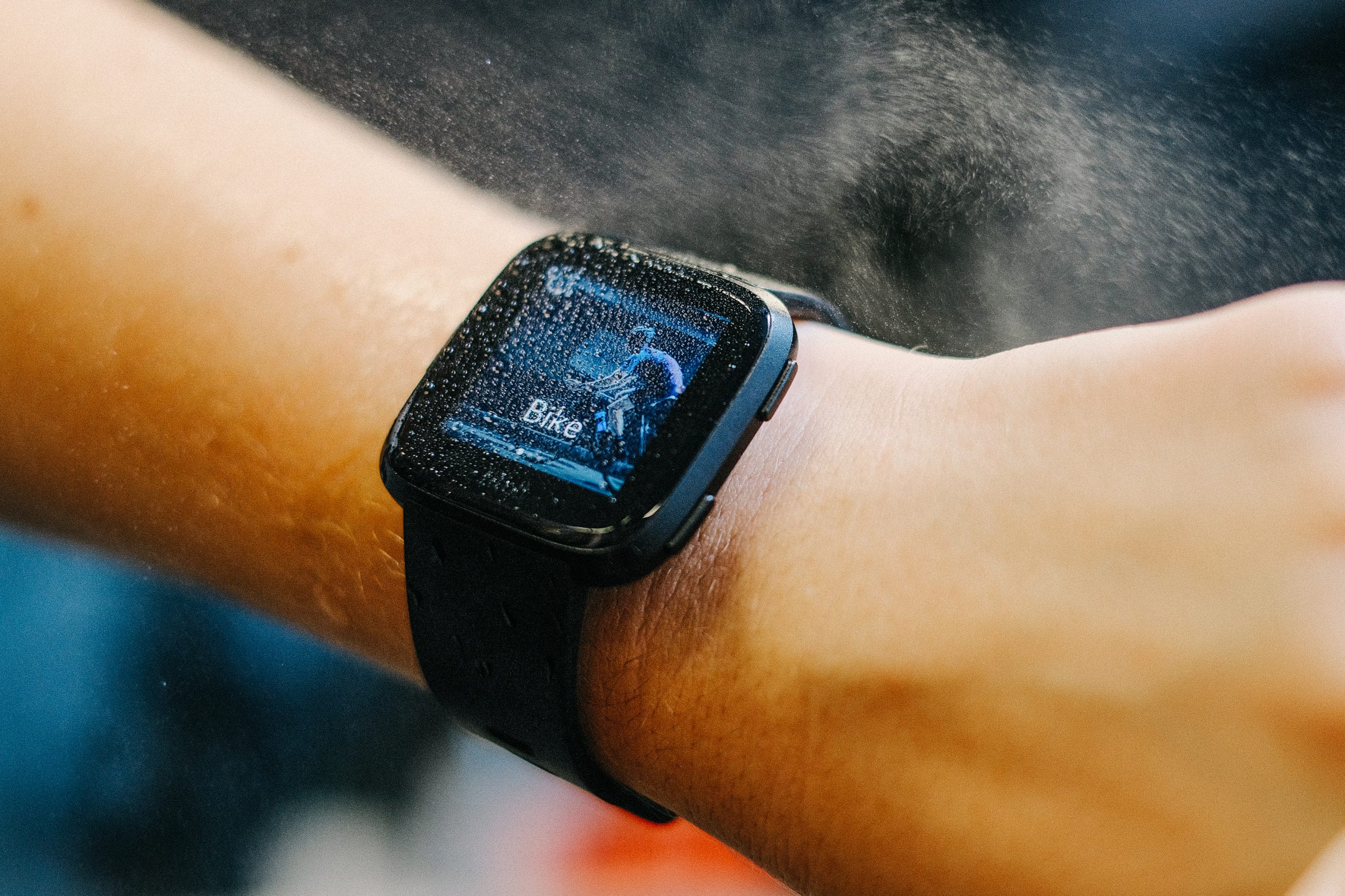 Montre connectée Fitbit Versa noire au poignet, écran couvert de gouttes d'eau affichant « Bike »