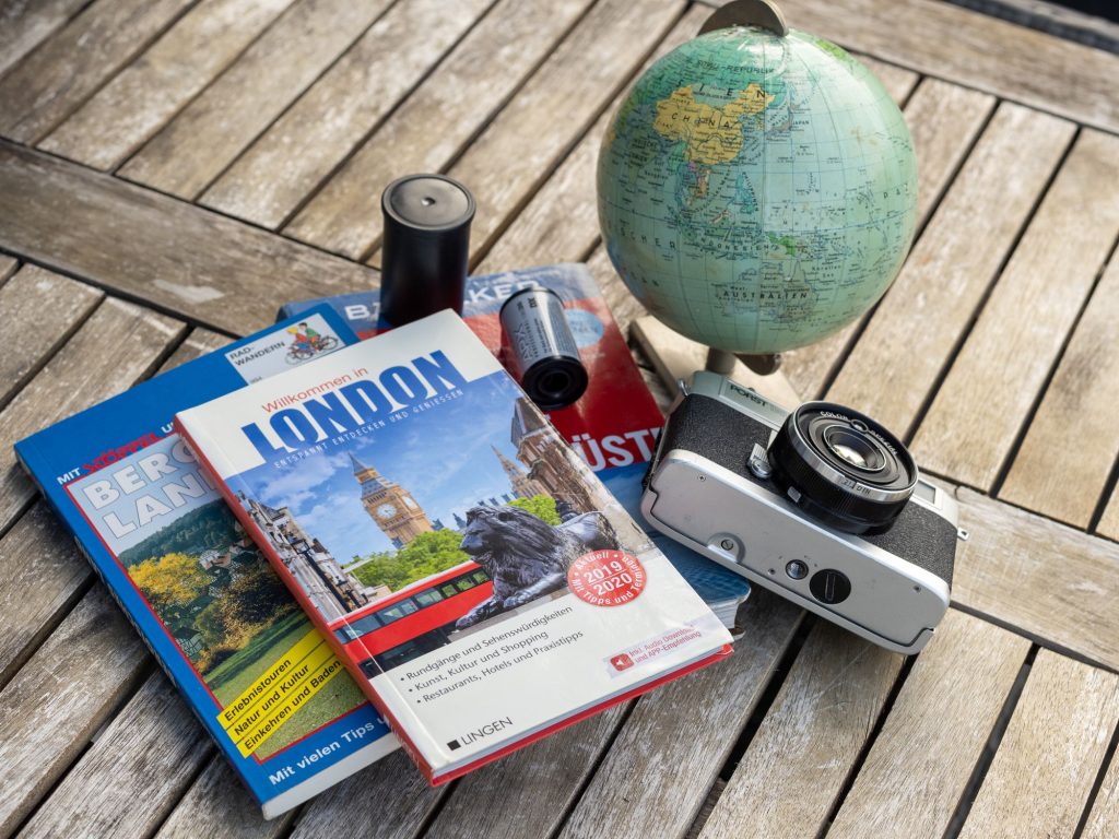 Guides de voyage, globe terrestre et appareil photo argentique posés sur une table en bois
