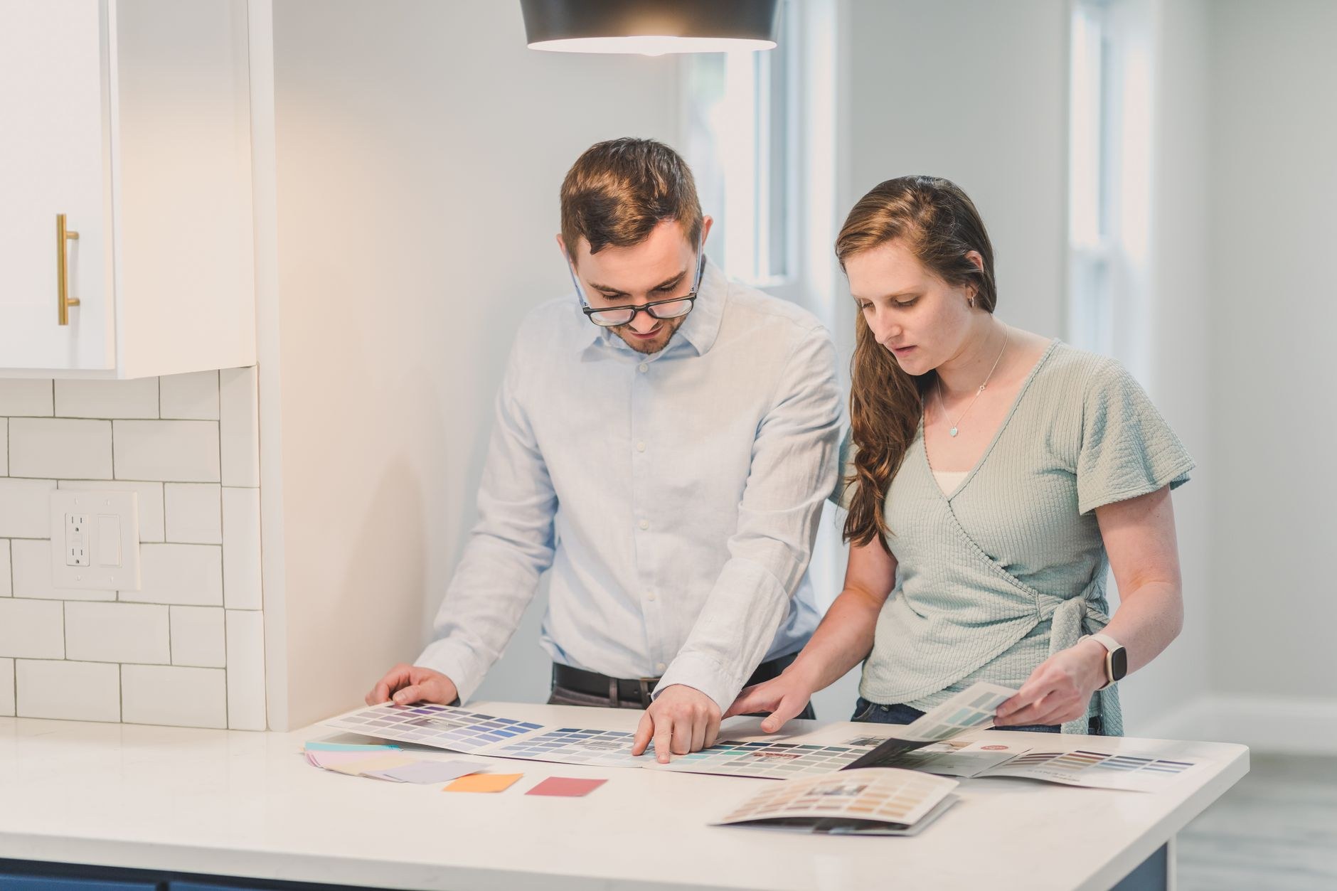 Un homme et une femme penchés sur un plan de travail de cuisine, pointant des nuanciers et des échantillons de couleurs étalés devant eux