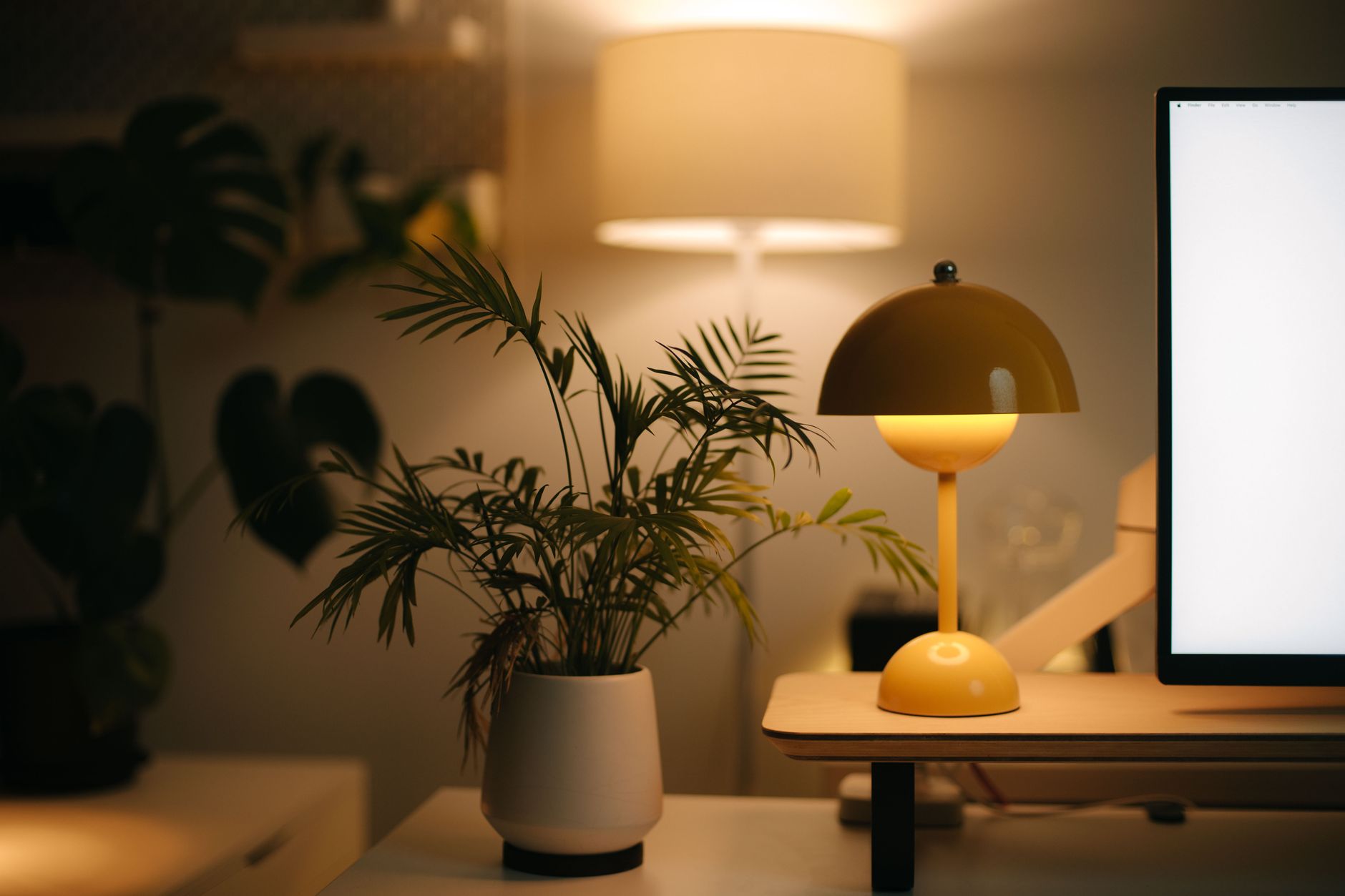 Petite lampe de bureau jaune allumée à côté d’une plante et d’un écran, dans une lumière chaude