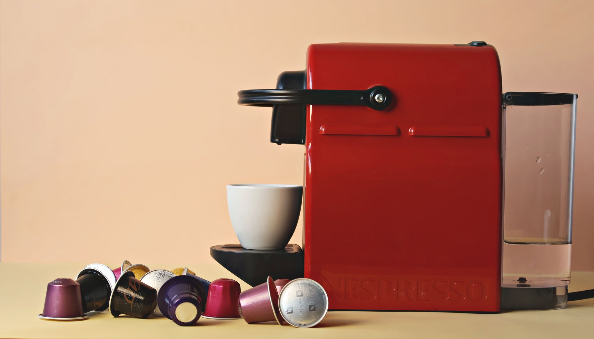 Machine à café à capsules rouge entourée de capsules colorées et d'une tasse