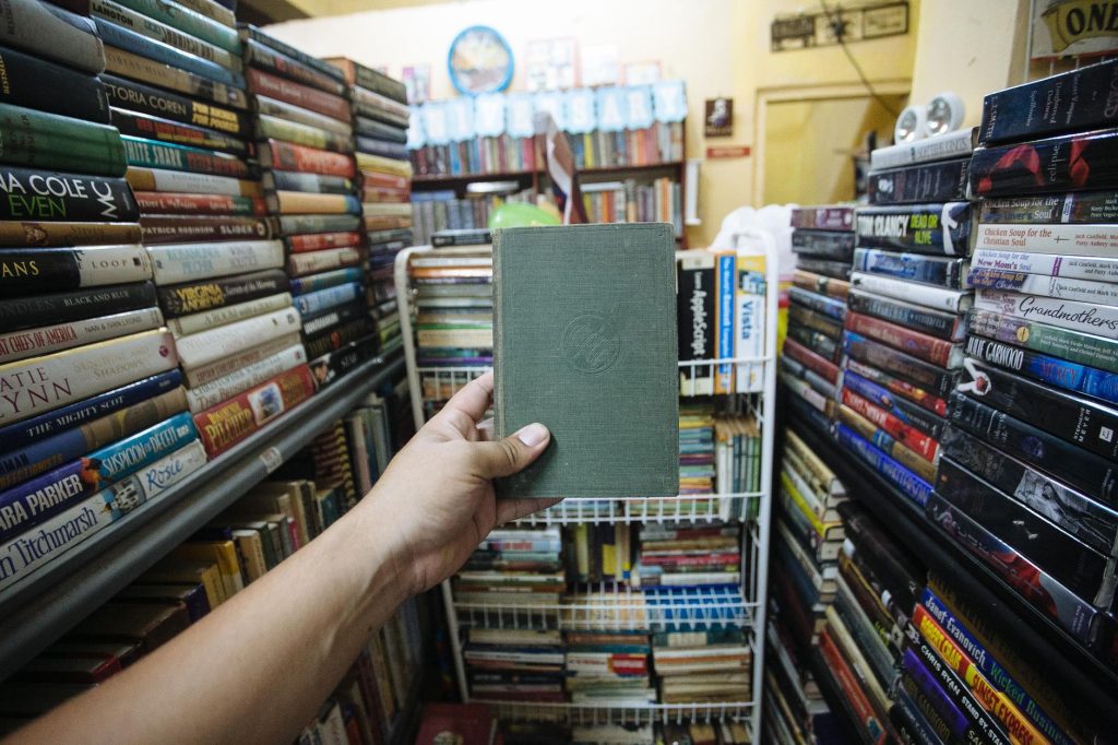 Main tirant un petit livre de poche d'une étagère remplie de livres