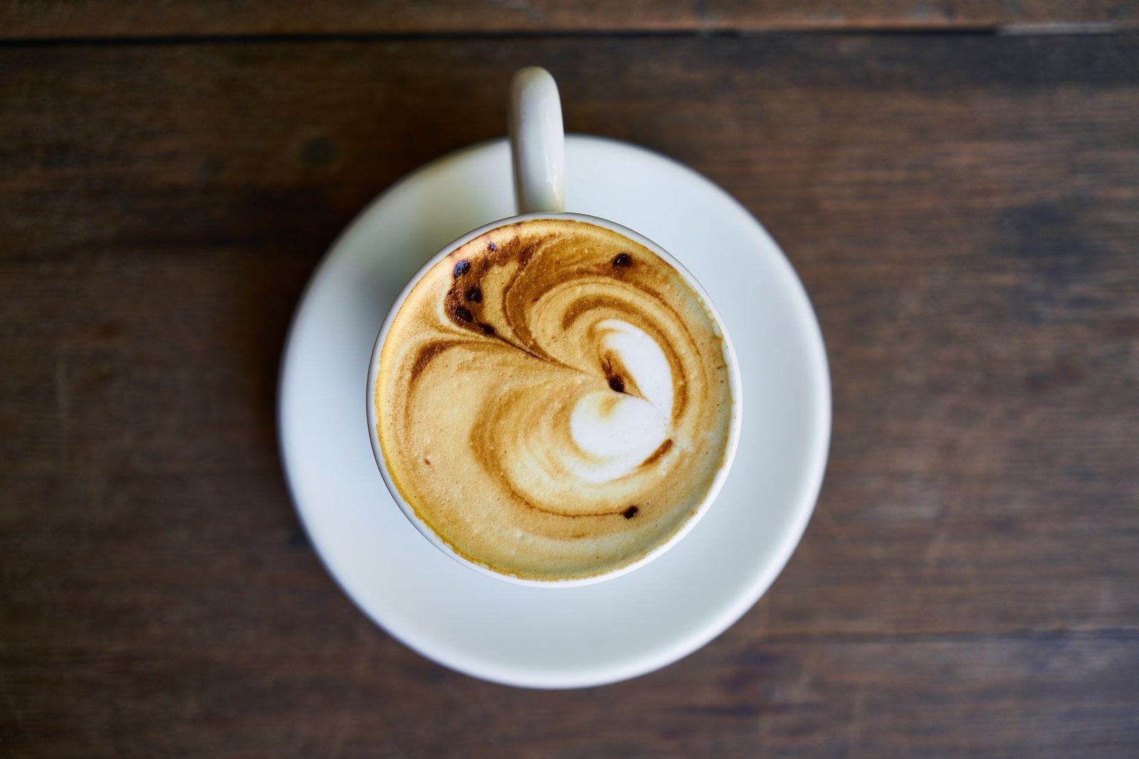 Tasse de cappuccino vue de dessus, avec de la mousse de lait dessinée en spirale, sur une table en bois sombre