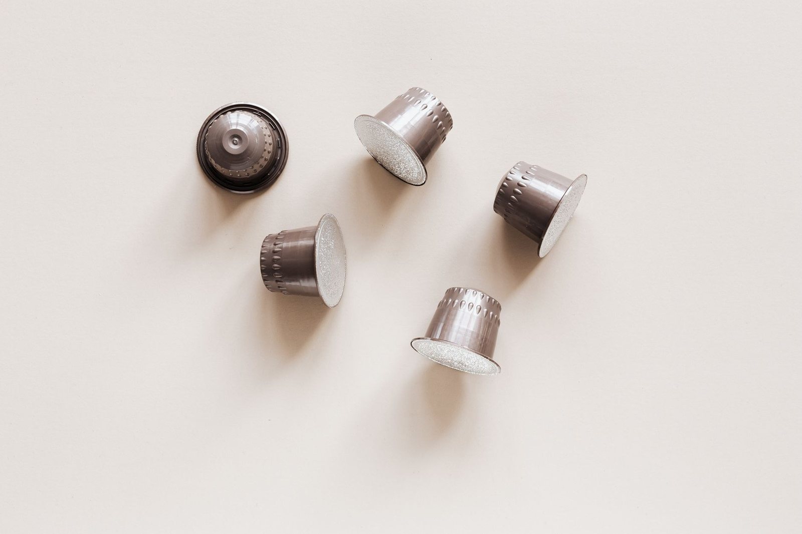 Cinq capsules de café en aluminium posées sur un fond clair, vues de dessus et de côté