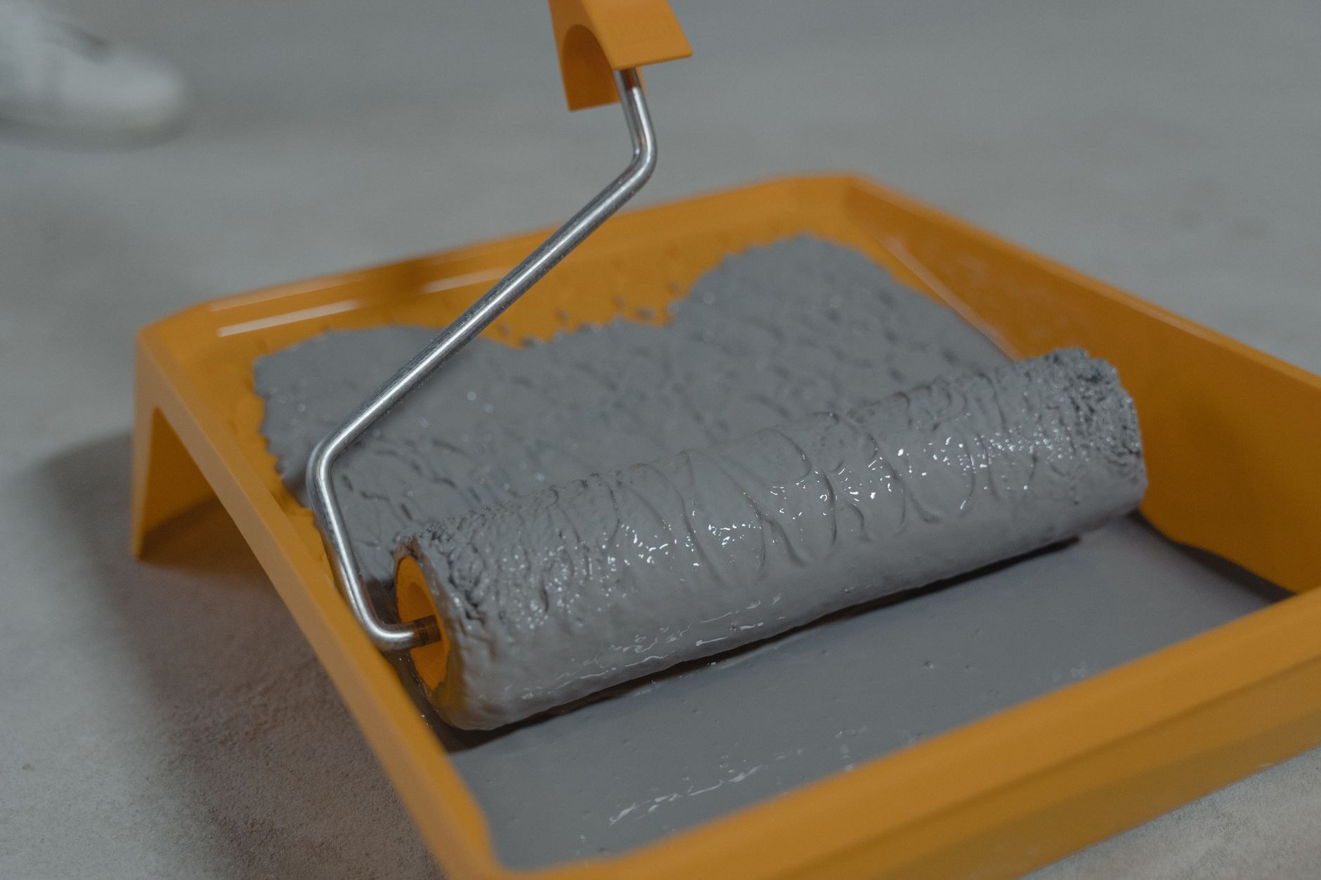 Rouleau à peindre chargé de peinture grise, posé dans un bac à peinture orange