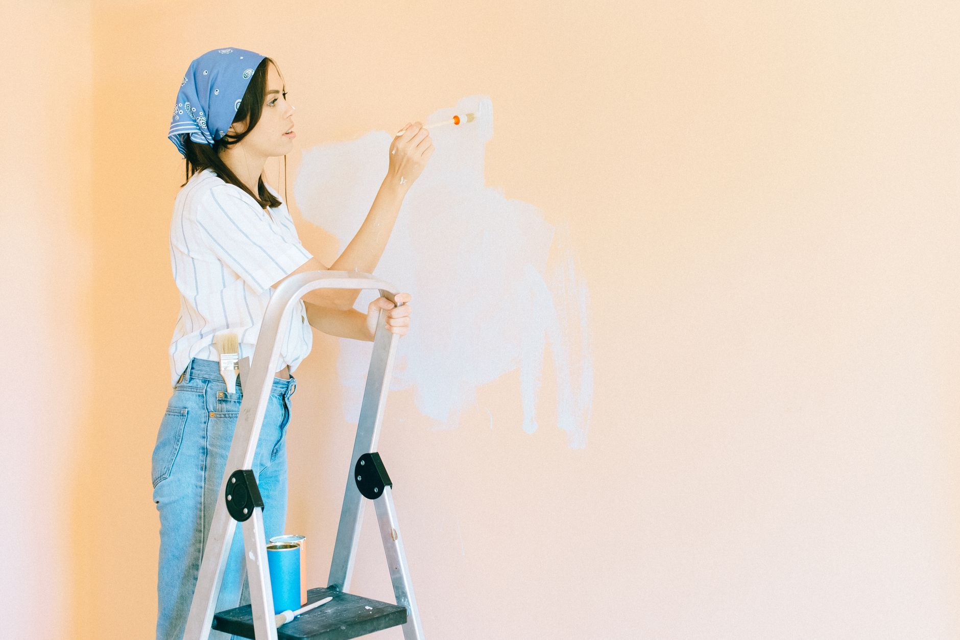 Femme sur un escabeau qui peint à la main une zone blanche sur un mur couleur pêche