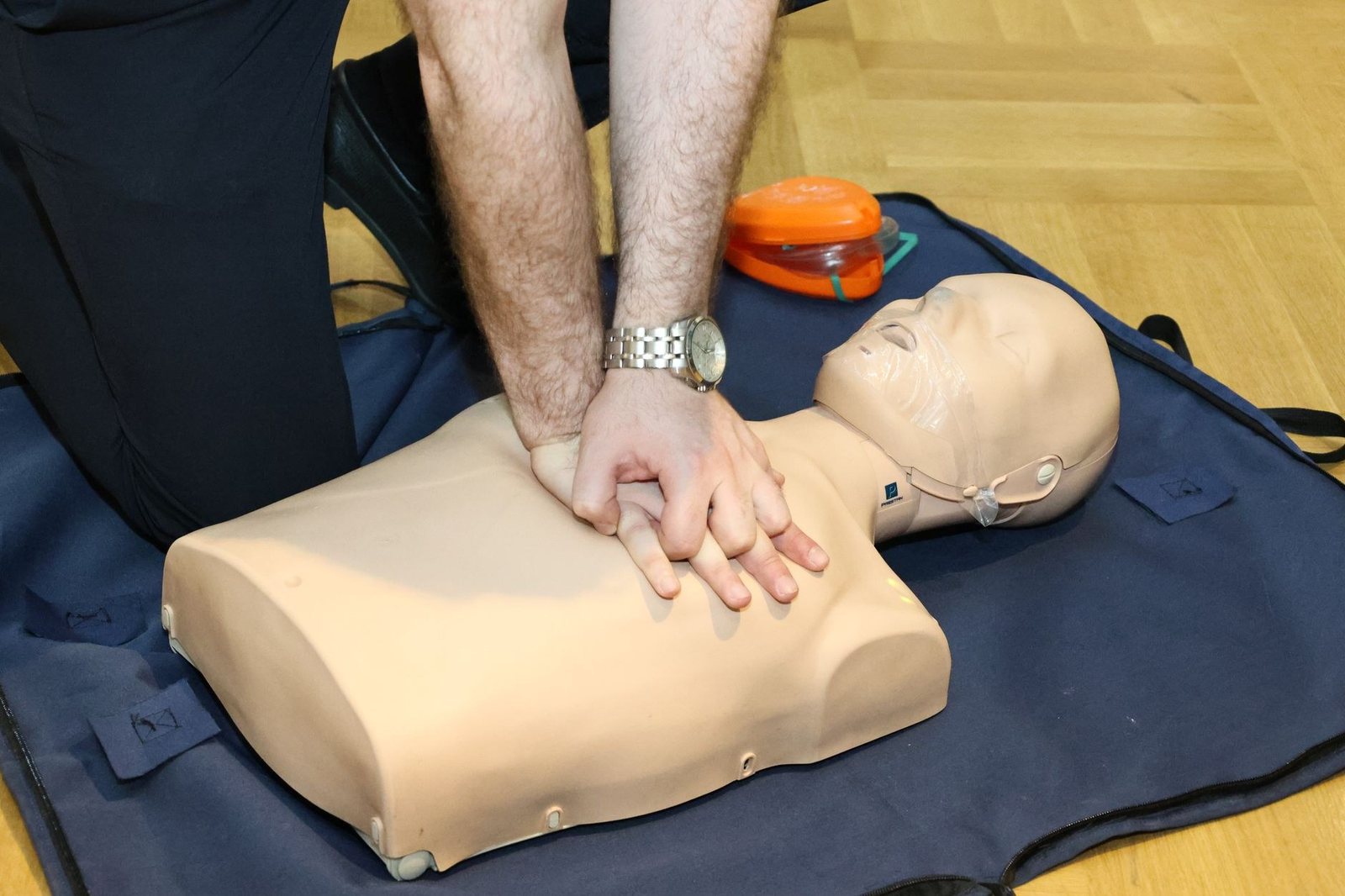 Deux mains superposées appuyant sur le thorax d’un mannequin de formation, à genoux sur un tapis, lors d’un exercice de massage cardiaque
