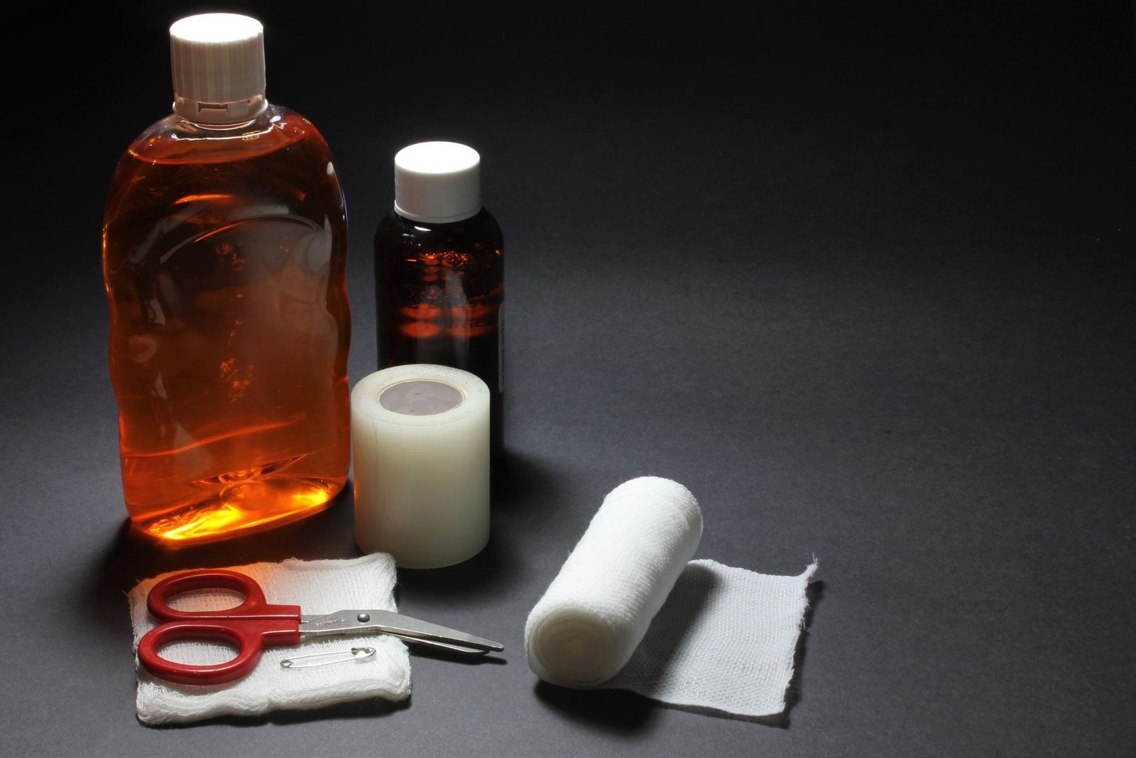 Matériel de premiers secours posé sur une table sombre : flacon d’antiseptique, compresses, bande de gaze, ruban adhésif et ciseaux à bouts ronds
