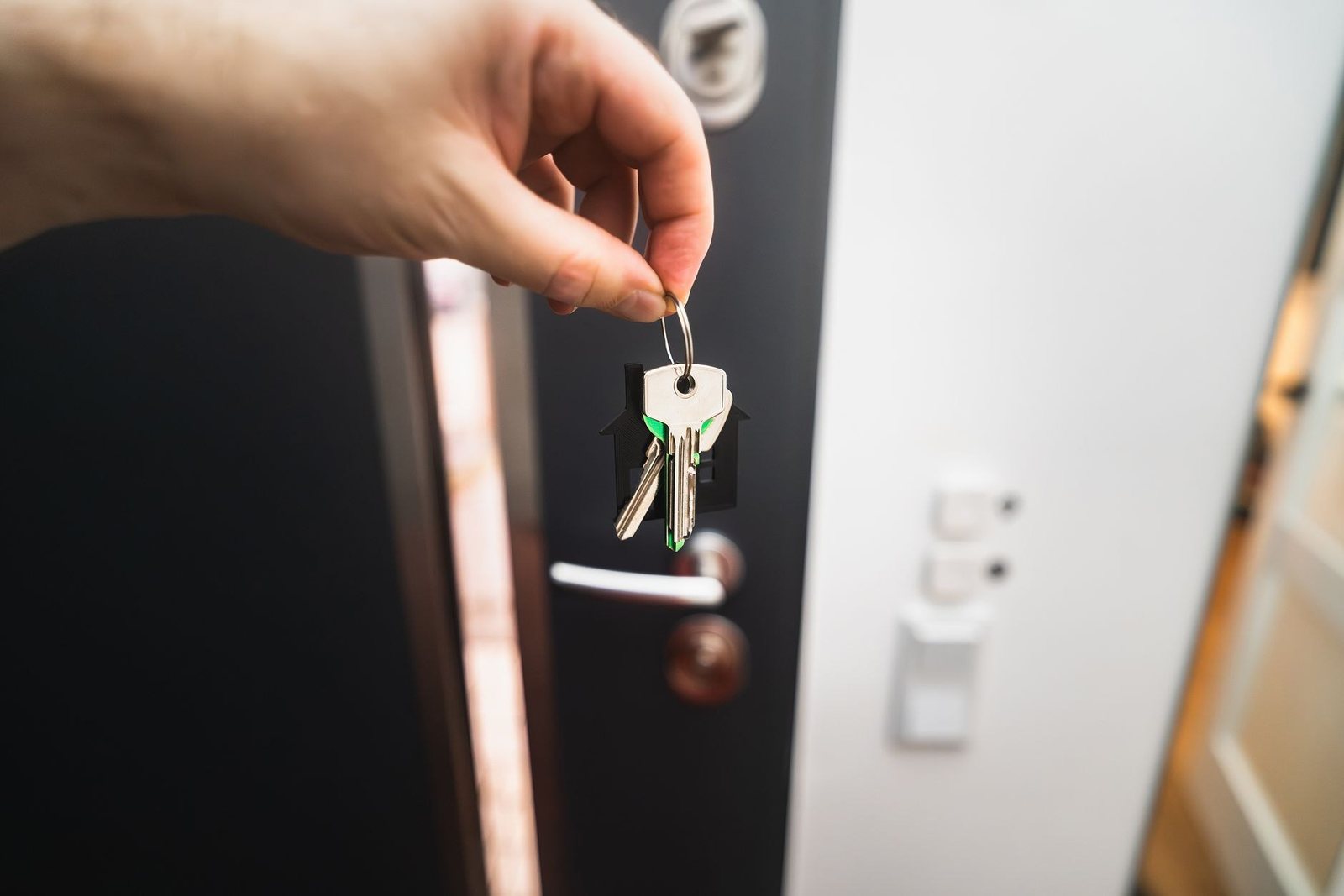 Une main tient un trousseau de clés avec un porte-clés en forme de maison devant la serrure d’une porte d’entrée