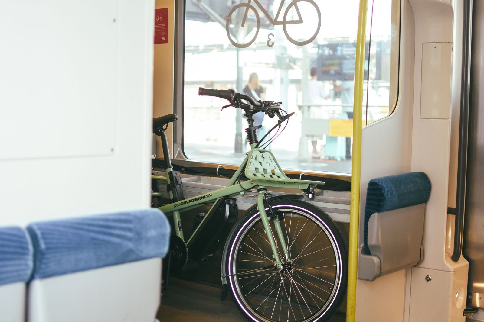 Vélo vert accroché dans l’espace dédié d’une rame de train, devant une fenêtre donnant sur le quai