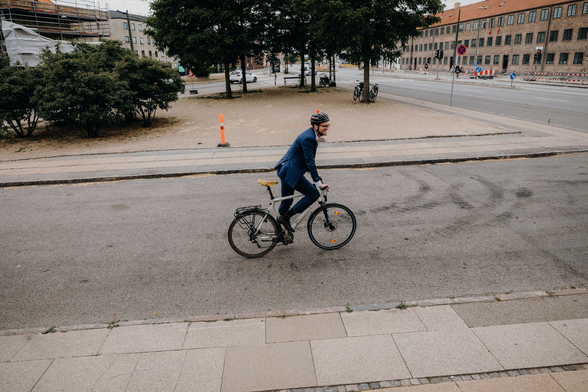 Un cycliste en costume bleu et casque roule sur une rue vide d'une ville, avec une piste cyclable sur le côté
