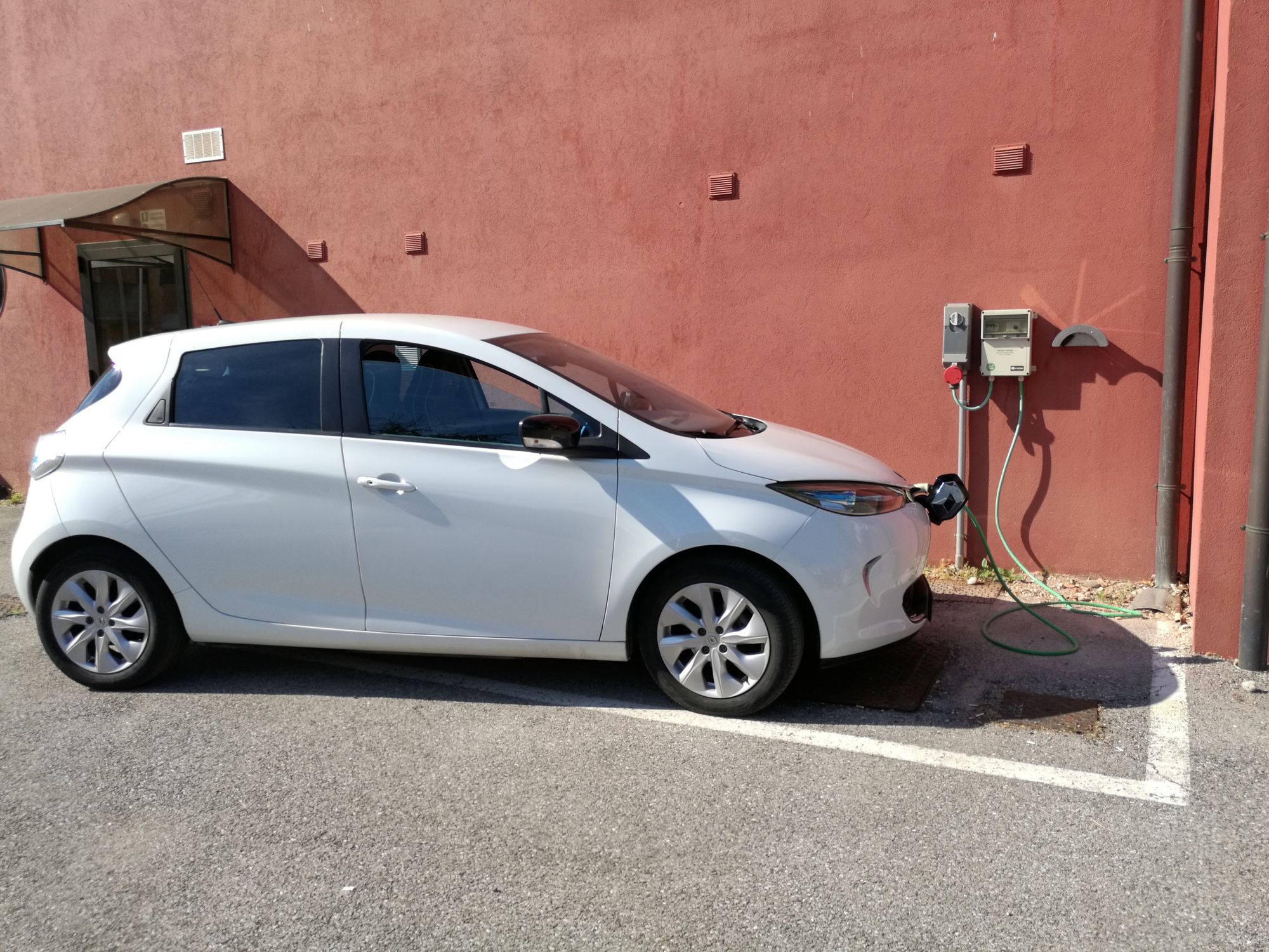 Petite voiture électrique blanche branchée à une borne de recharge contre un mur