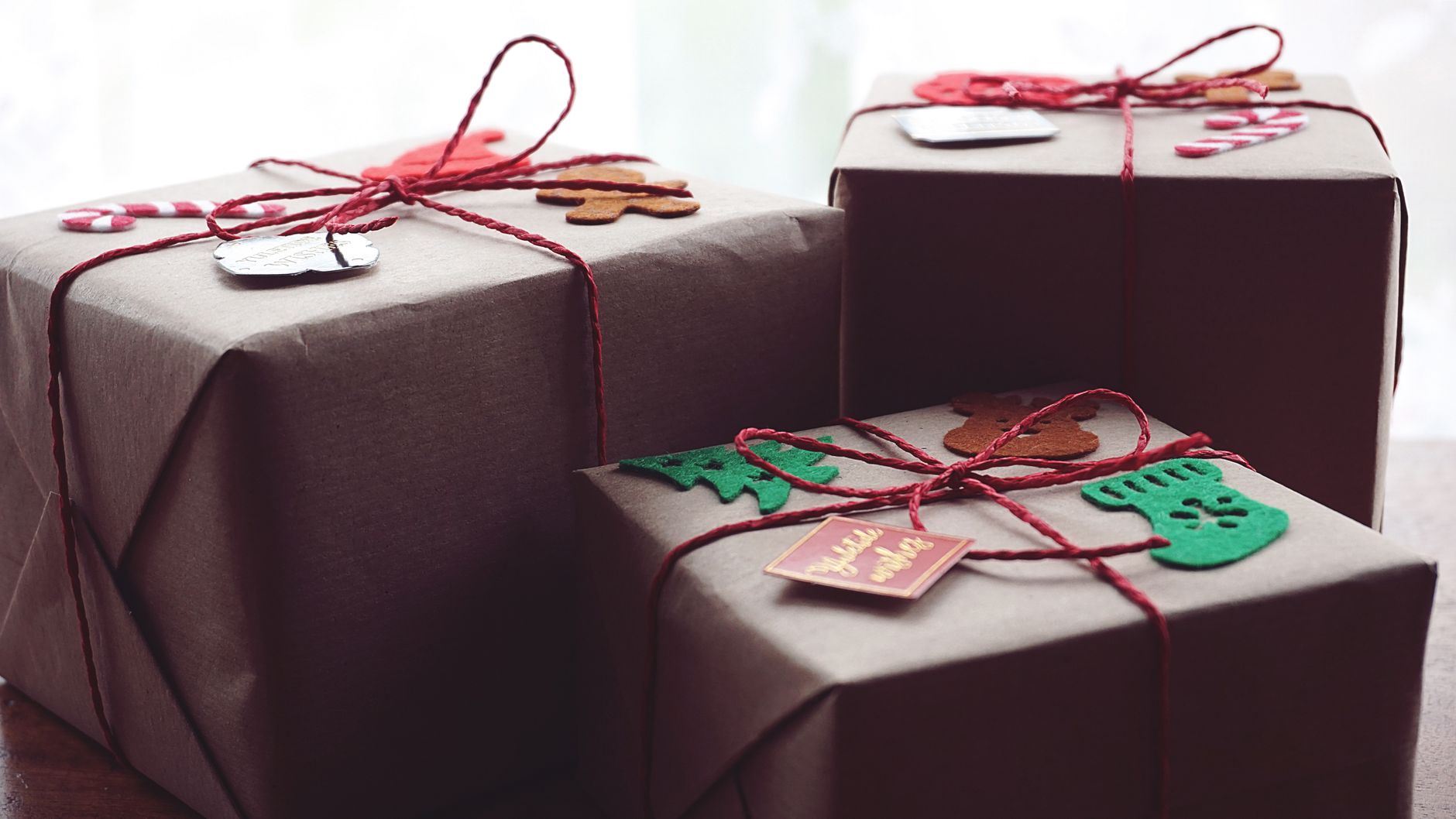 Trois cadeaux emballés dans du papier kraft, noués de ficelle rouge et décorés de petites figurines en feutre