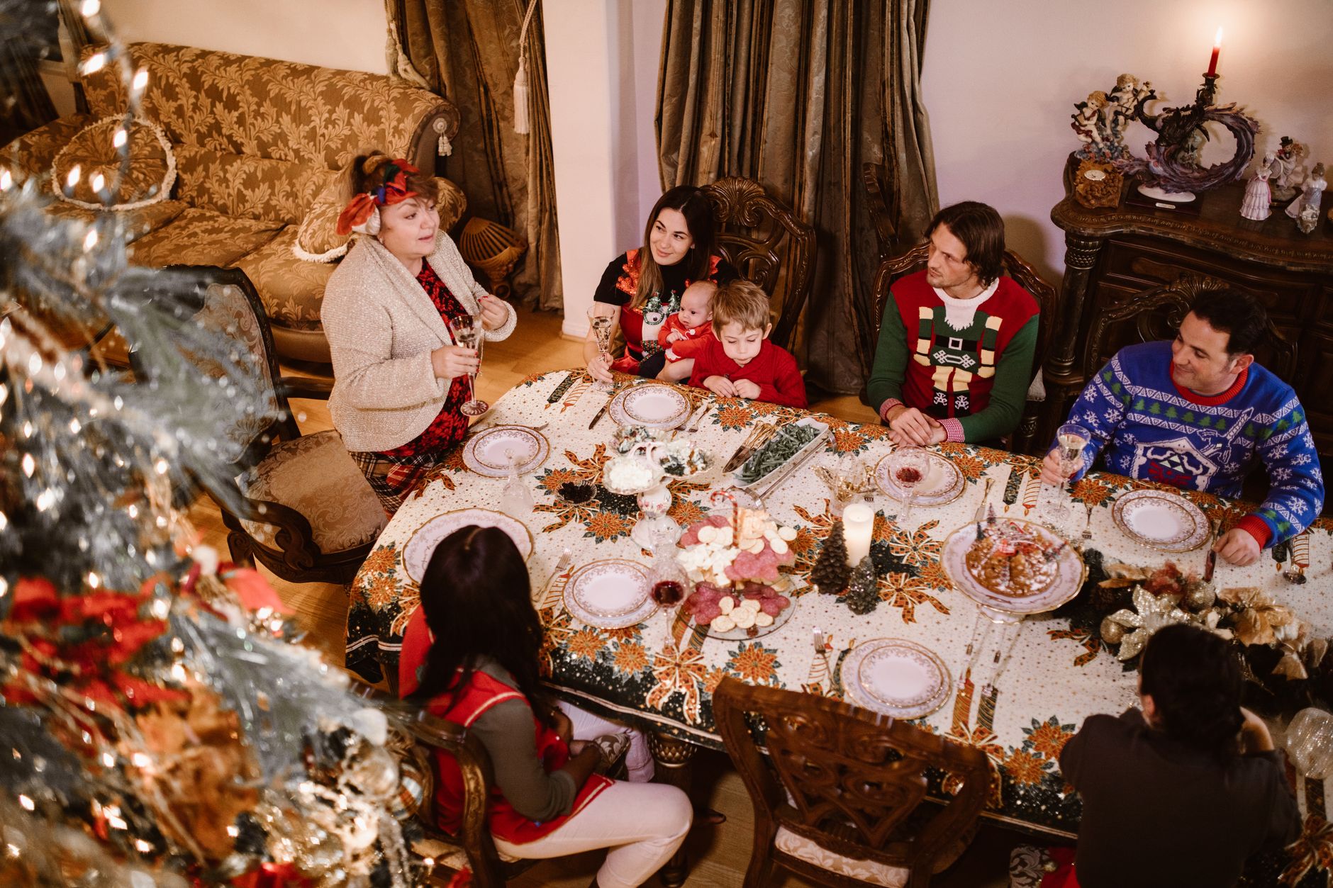 Famille réunie autour d’une table dressée pour le repas de Noël, avec un sapin décoré au premier plan