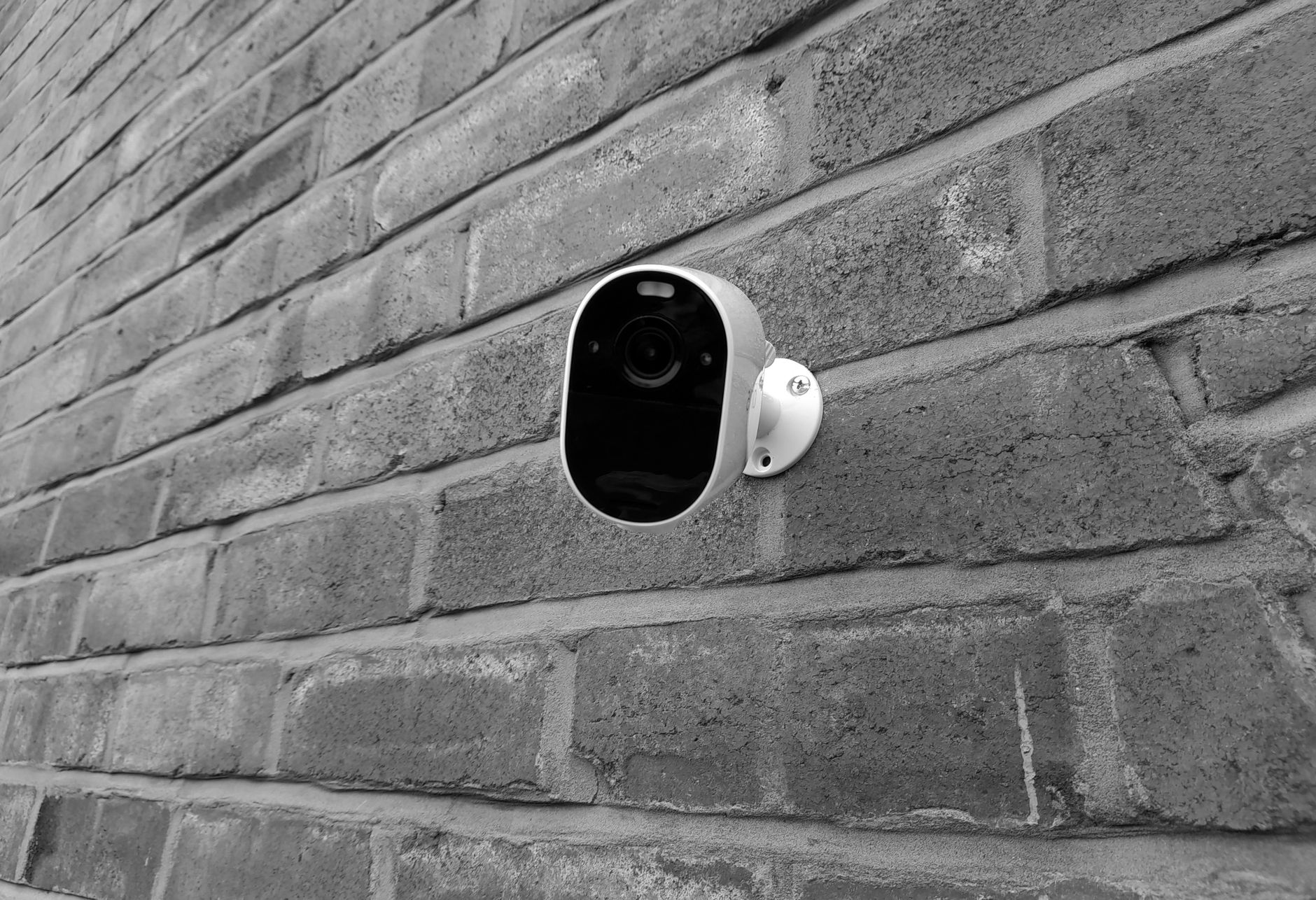 Petite caméra sans fil blanche et noire fixée sur un mur de briques