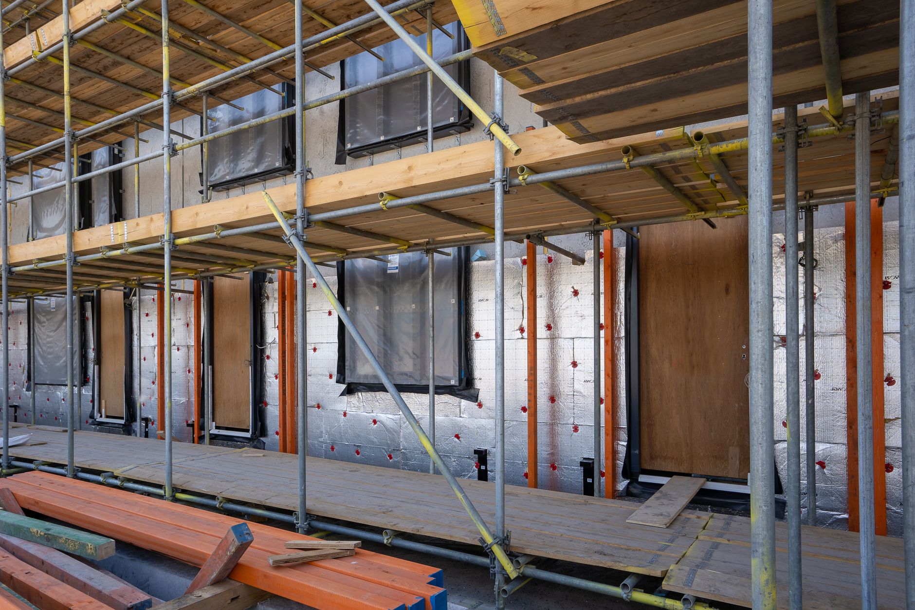 Façade d’un bâtiment en travaux sous échafaudage, avec des panneaux isolants argentés fixés au mur autour des fenêtres