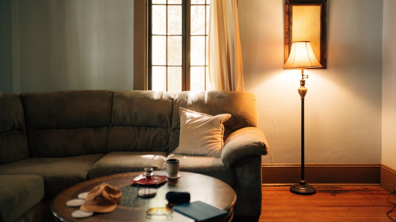 Lampadaire à abat-jour allumé dans un salon aux murs clairs, à côté d'un canapé et d'une table basse