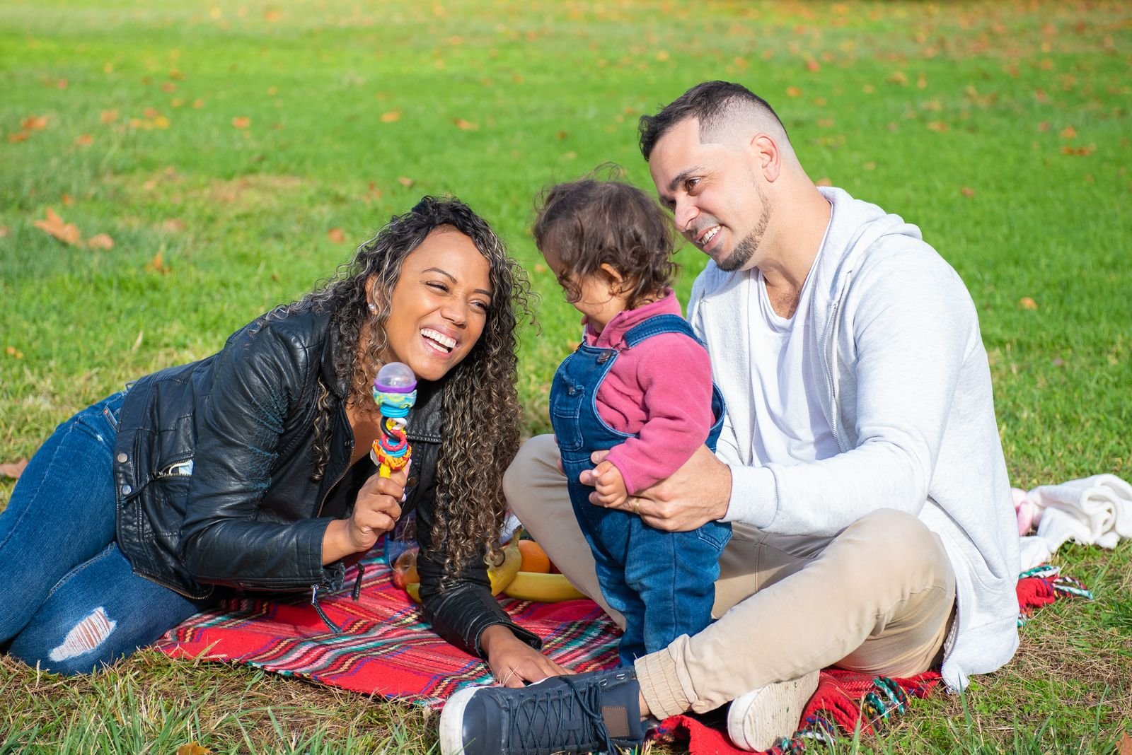 Une famille de trois personnes pique-niquant sur une couverture rouge dans l'herbe d'un parc en automne