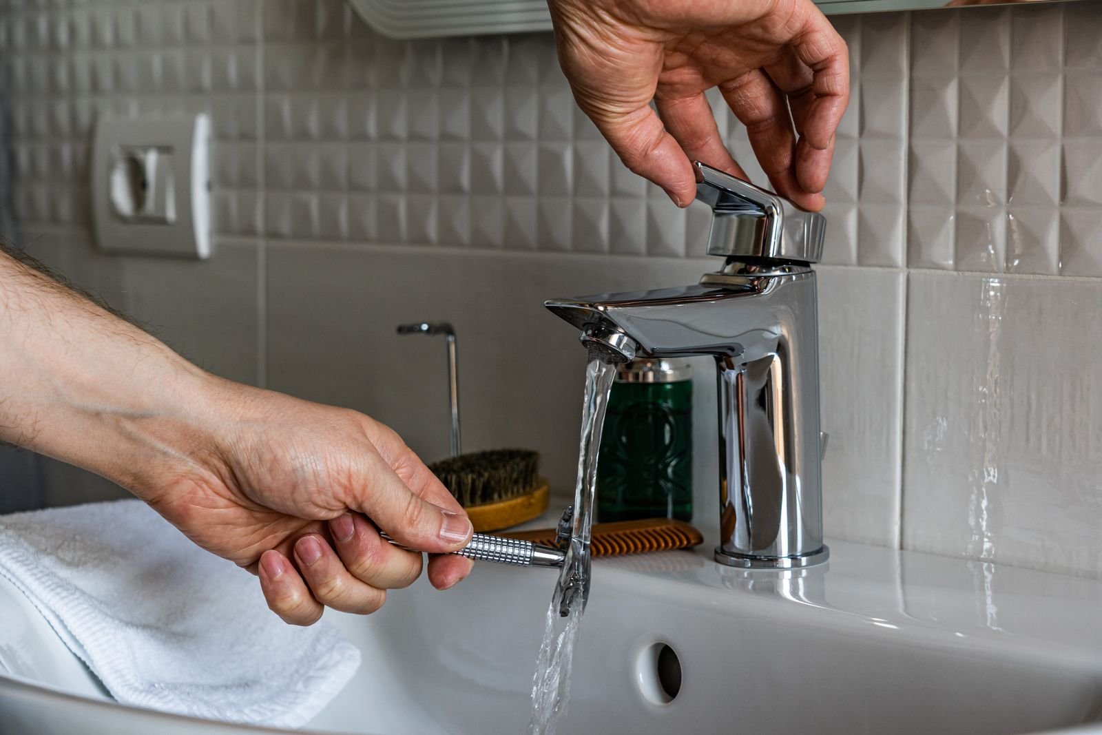 Eau qui coule d'un mitigeur de lavabo pendant qu'une personne se rase